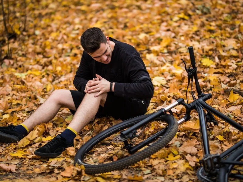Cyclist sitting on the ground holding an injured knee after a fall