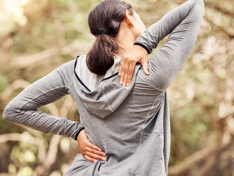 Person holding their lower back in pain outdoors